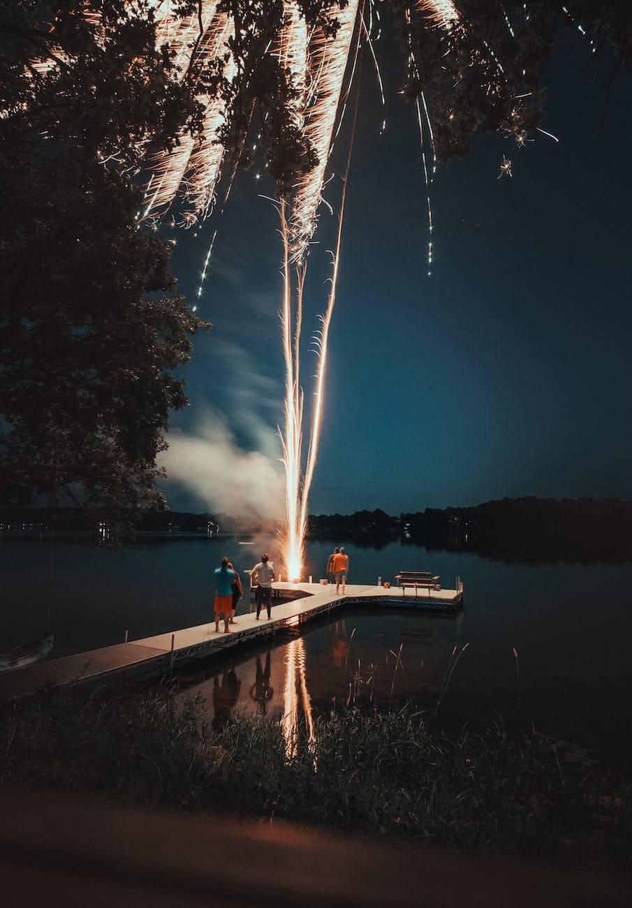 photo of people standing on white dock watching fireworks during nighttime